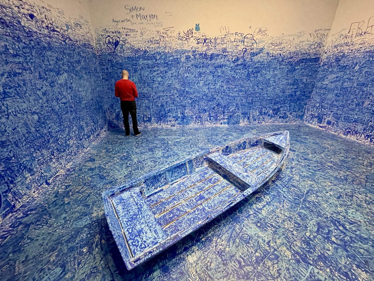 An art installation: a room papered floor to ceiling in handwriting, with a small boat at its center