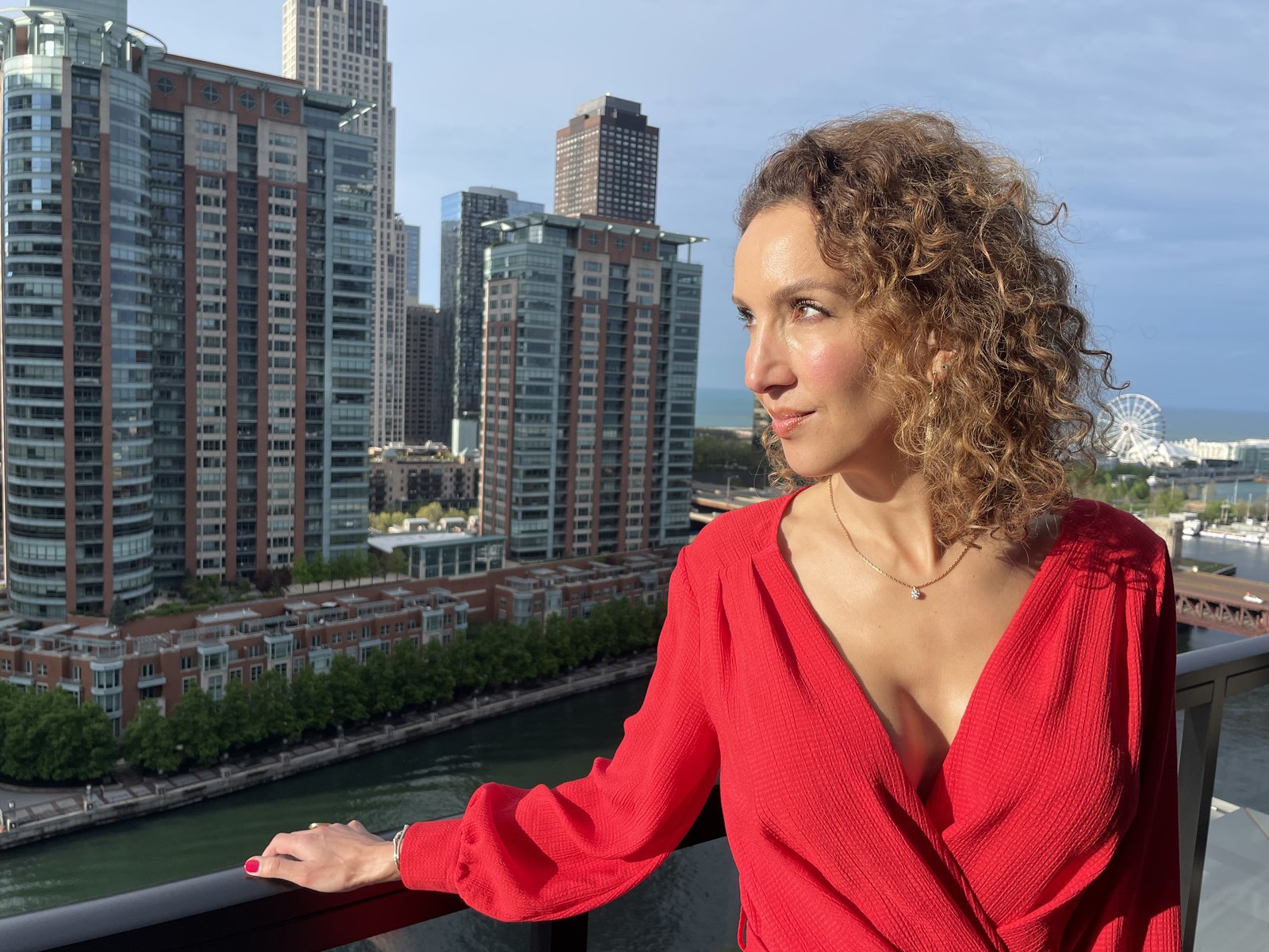 A woman in a red blouse on a balcony overlooking the Chicago River and skyline.